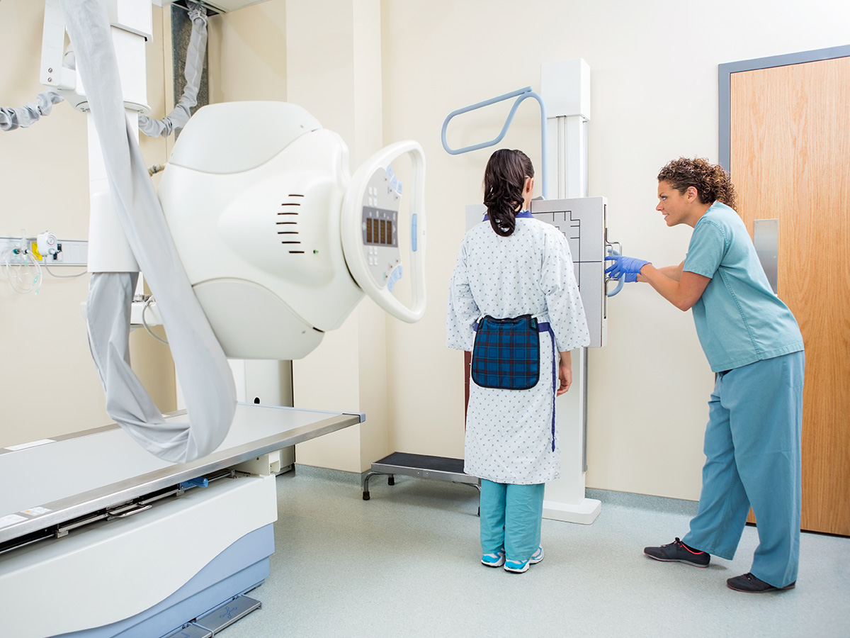 A nurse adjusting an x-ray machine for a female patient in the examination room.