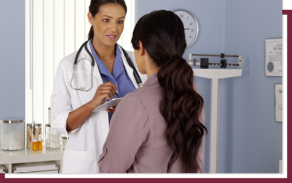 A female doctor talking to a woman who is sitting in her medical office.