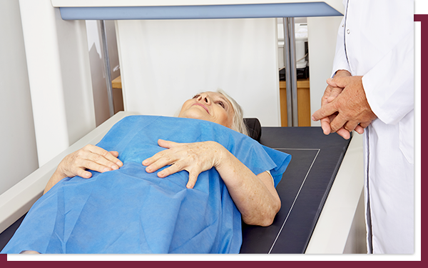 A woman laying on a DEXA scan table in a hospital gown with a doctor standing next to her.
