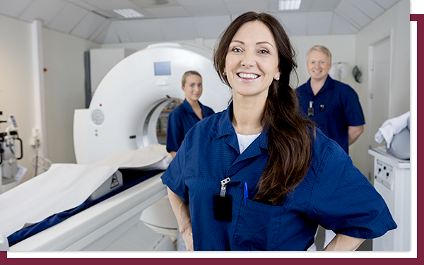 Three medical technicians standing in front of an MRI machine and smiling.