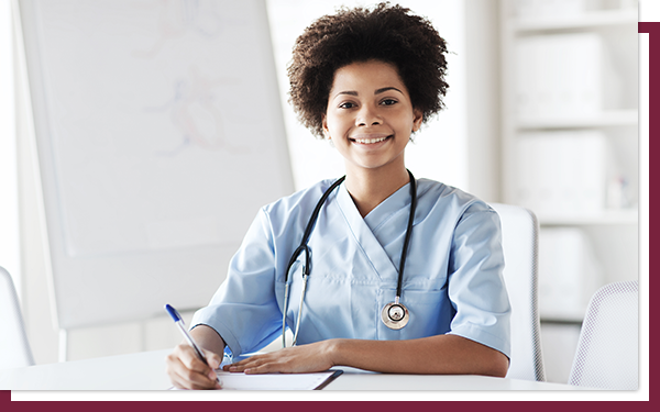 A happy female doctor smiling for the camera with a pen and medical pad on her desk.