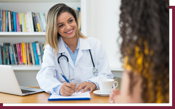 A young female doctor smiling at a patient while making notes on her writing pad.