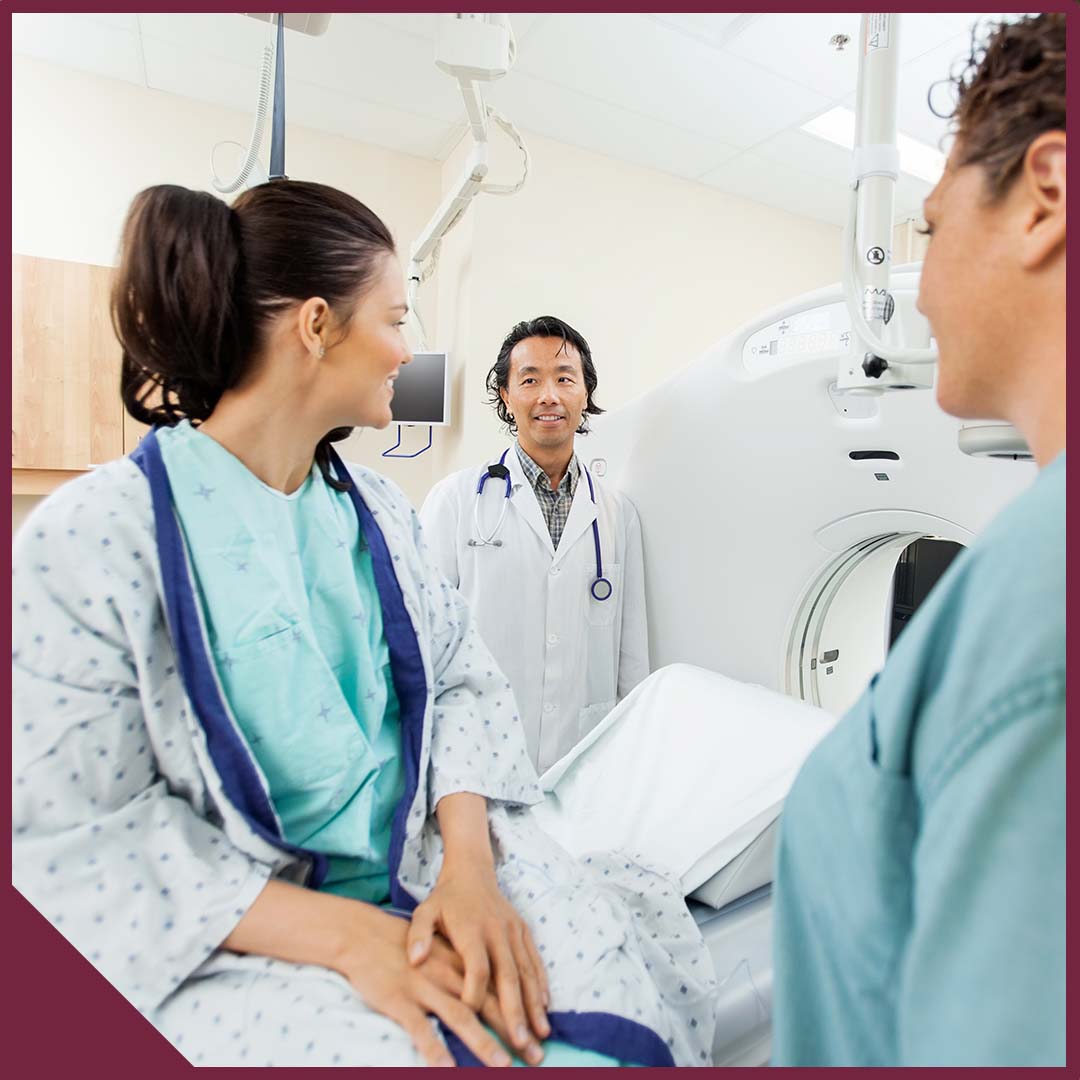 A woman sits on an imaging table speaking with a doctor and a nurse.