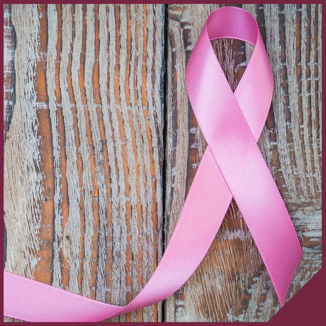 A pink breast cancer awareness ribbon sitting on a wood background.