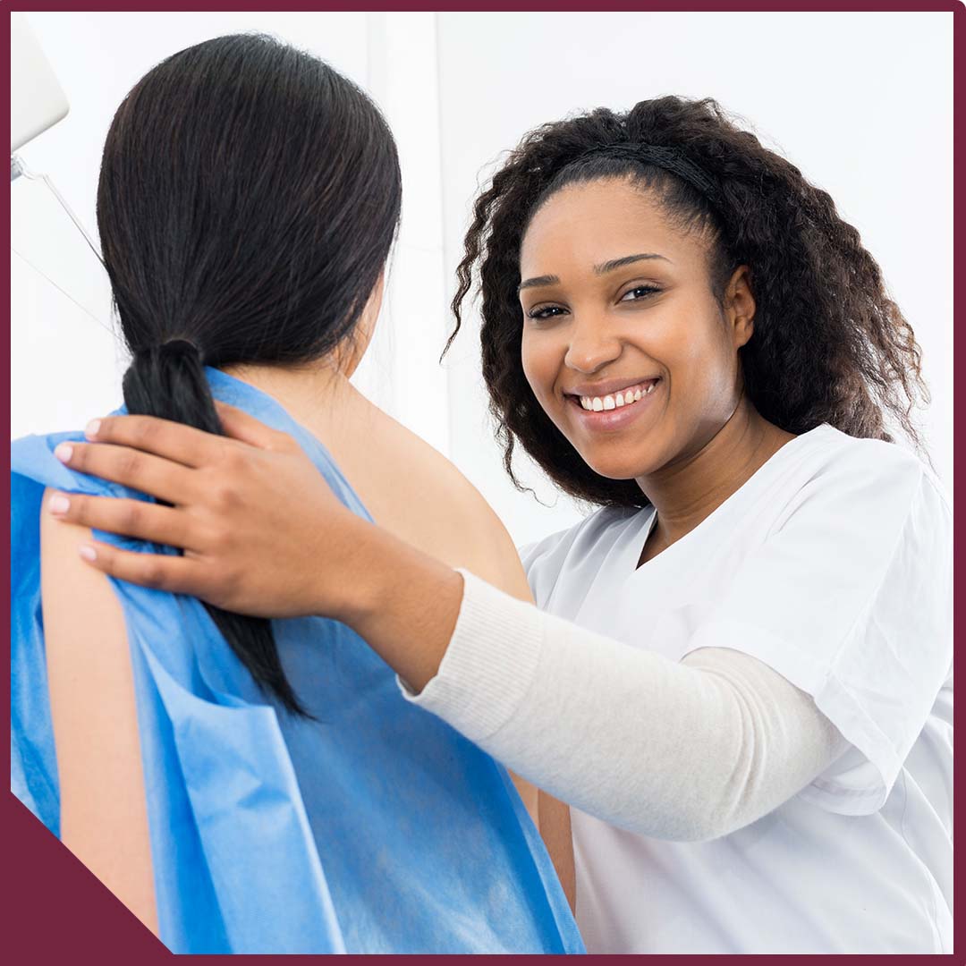 A female patient in a gown with her back turned and a smiling doctor looking at the camera.