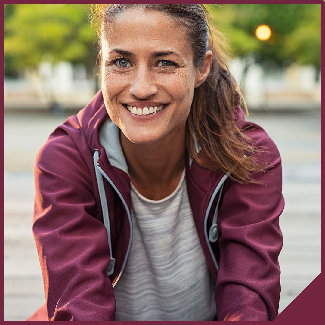 A healthy middle aged woman taking a break from her run and smiling at the camera.