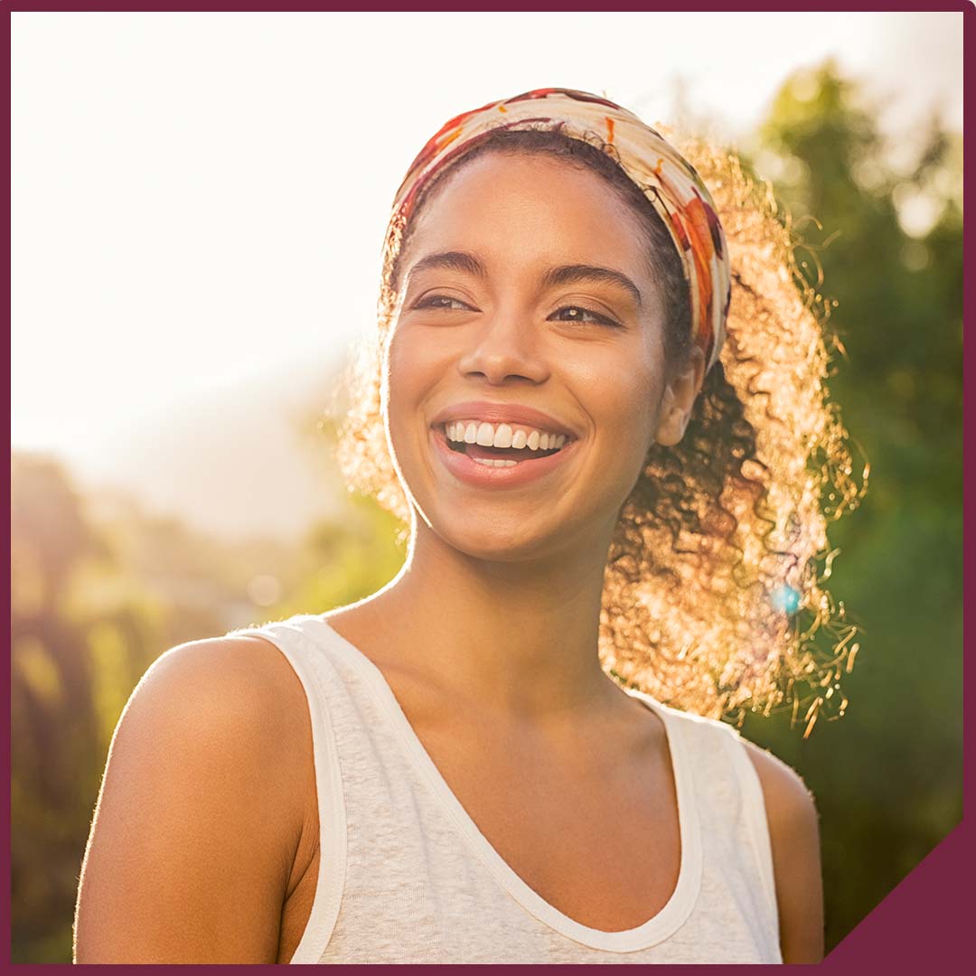 Portrait of a smiling young woman with the sun shining behind her.