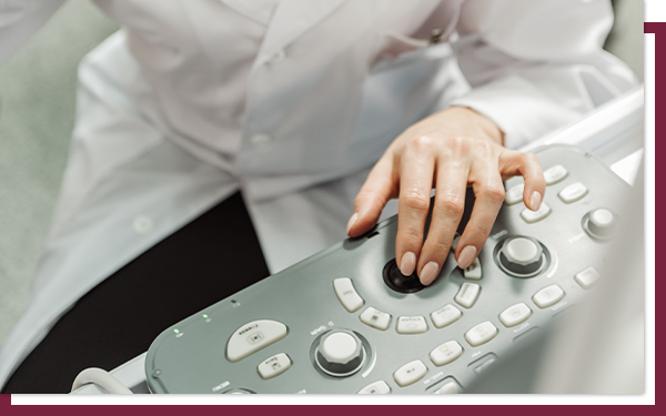 Confident doctor sitting at keyboard of ultrasound machine with a smile.