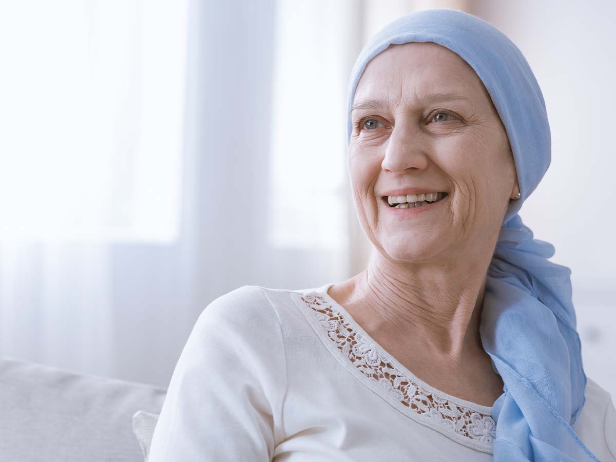 An older woman wearing wrap on her head and smiling from the hospital bed.