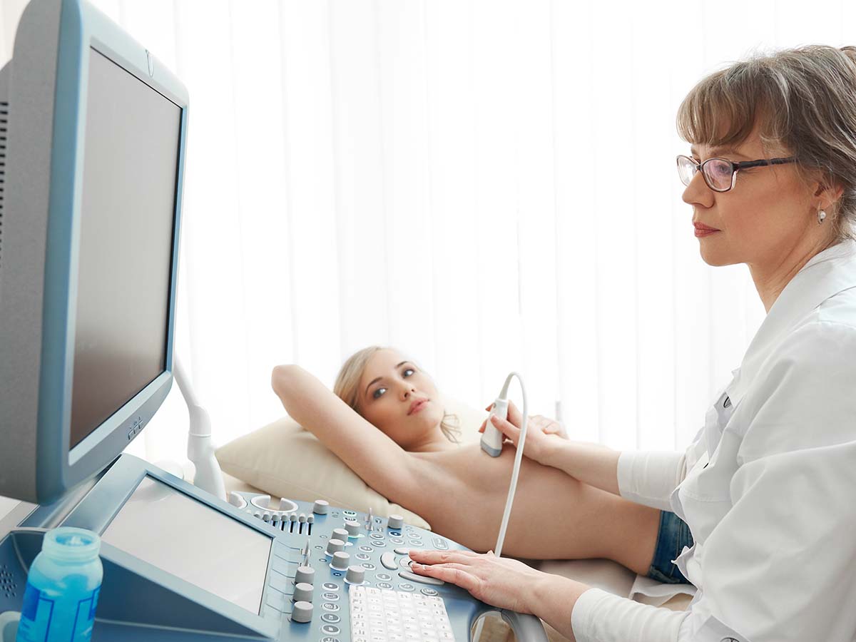 Female doctor performing a breast ultrasound on a middle-aged patient.