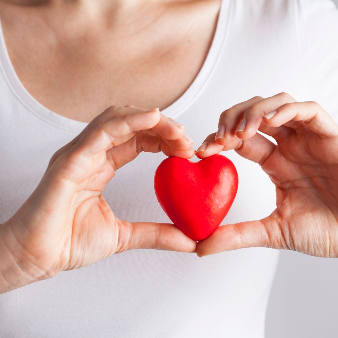 A woman holding a red heart over her chest.