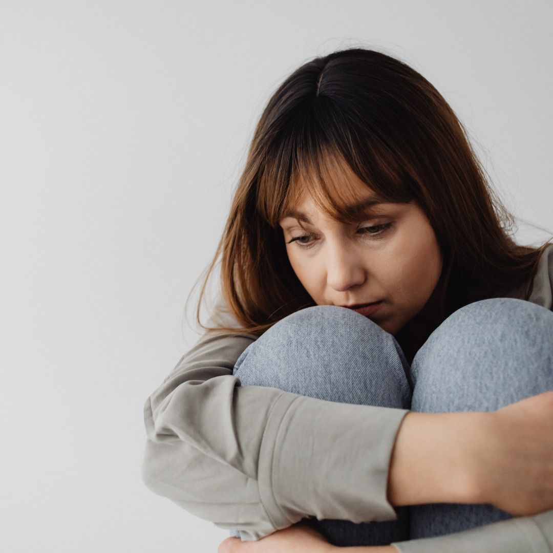 A woman hugging her knees and looking down.