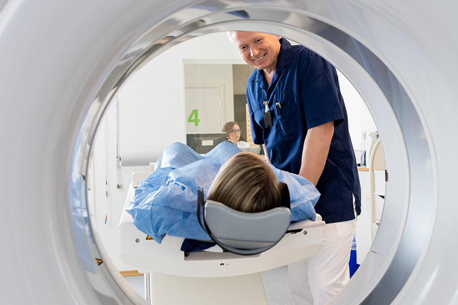a person laying on an MRI bed with a nurse assisting
